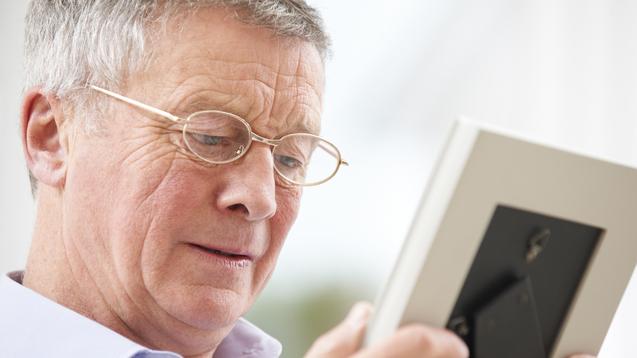 Ein älterer Mann mit Brille betrachtet ein Foto in einem Bilderrahmen.